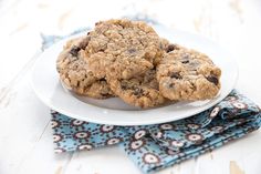 two oatmeal chocolate chip cookies on a white plate with blue napkins