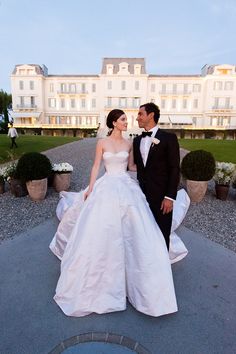 a man and woman in formal wear standing next to each other on a walkway near some bushes