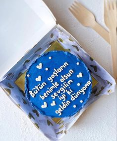 a blue cake with white frosting in a box on a table next to utensils