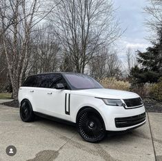 the white range rover is parked in front of some trees and bushes with black rims