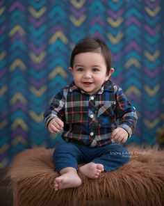 a baby boy sitting on top of a furry stool in front of a colorful wall