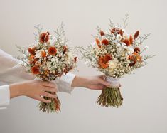 two brides hands holding bouquets of white, orange and brown flowers with greenery