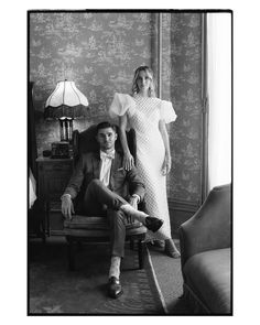 black and white photograph of man and woman sitting in chair with lamp on wall behind them