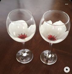 two wine glasses sitting on top of a wooden table next to each other with white flowers in them