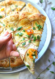 a person holding a slice of pizza with toppings on it, in front of a plate