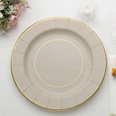 a white plate with gold trim on top of a table next to flowers and candles