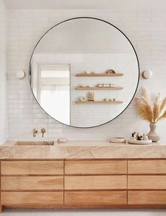 a bathroom with a large round mirror above the sink and wooden drawers on the side