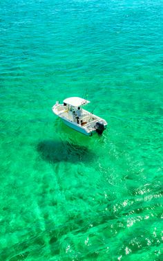 a small white boat floating on top of clear blue water next to a shore line