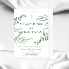 a white wedding card with green leaves and a cross on the front is laying on a bed