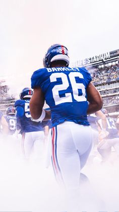 two football players walking onto the field in uniforms with numbers painted on them and people watching from the stands