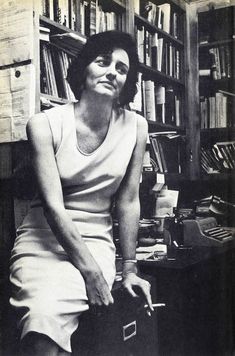 black and white photograph of a woman sitting in front of a bookshelf holding a suitcase