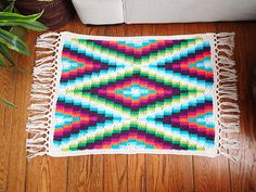 a multicolored rug with fringes on the floor next to a potted plant