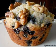 a muffin with blueberries and walnuts on top sitting on a white plate