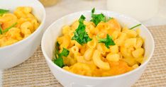 two white bowls filled with macaroni and cheese on top of a place mat