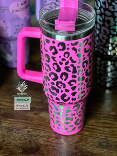 pink and green leopard print travel mug with lid on wooden table next to other cups