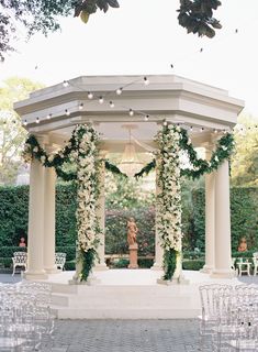 an outdoor wedding setup with white flowers and greenery on the pillars, surrounded by chairs