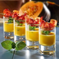 four shot glasses filled with orange juice and garnished with bacon