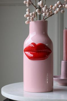 a pink vase with red lips painted on it and some white berries in the background