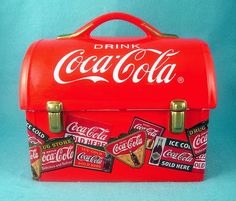 an old coca - cola lunch box with stickers on the lid is shown in front of a blue background