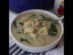 there is a bowl of soup with spinach and chicken in it on the table