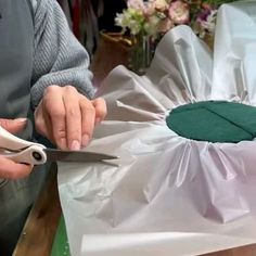 a person cutting fabric on top of a table with scissors and flowers in the background