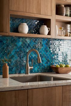 a kitchen sink with blue tiles on the backsplash and wooden cabinets above it