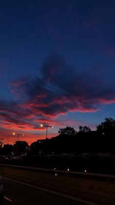 the sun is setting behind some clouds in the sky and cars are parked on the side of the road