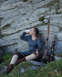 a woman sitting on the ground drinking from a cup