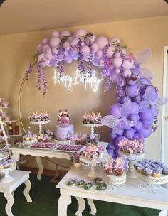 a table topped with lots of cakes and cupcakes covered in purple frosting