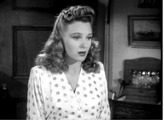 a woman in a polka dot shirt is looking at the camera while standing next to a dresser