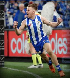 a male afl player is running with his arms wide open in celebration after kicking the ball