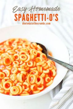 a white bowl filled with pasta and sauce on top of a striped towel next to a spoon