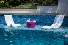 two lawn chairs sitting in the middle of a swimming pool next to an ice bucket