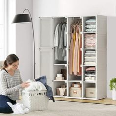 a woman sitting on the floor in front of a white closet with clothes and other items