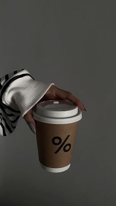 a woman's hand holding up a cup of coffee with the word % written on it