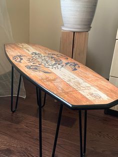 a wooden surfboard sitting on top of a metal stand next to a white vase