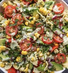 a bowl filled with pasta salad topped with tomatoes, corn and avocado dressing