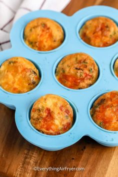 several muffins in a blue tray on top of a wooden table with a white towel