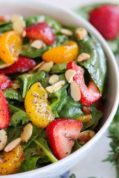 a salad with strawberries, oranges and almonds in a white bowl on a table