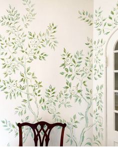 a chair sitting in front of a wall painted with green leaves