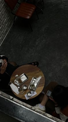 two people sitting at a table with their cell phones in front of them, looking down