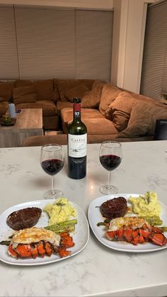 two plates of food and wine on a table in front of a couch with a bottle of wine