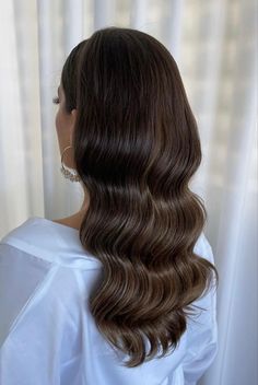 the back of a woman's head with long, wavy hair in front of a window