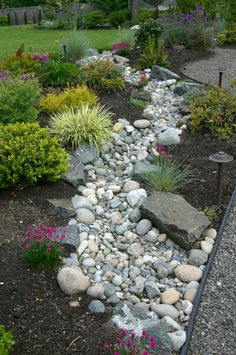 a garden with rocks and flowers in the center, along side a path that leads to a house