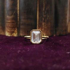 a gold ring with an emerald colored stone in the center on a purple velvet surface