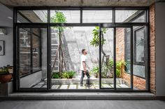 a person standing in an open room with glass walls and plants on the outside wall