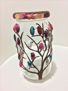 a glass vase decorated with colorful birds on a tree branch and ribbon tied around the top