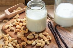 a wooden cutting board topped with cashews next to a glass of milk and cinnamon sticks