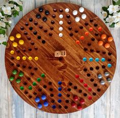 a wooden board game with several different colored dices on it and flowers in the background