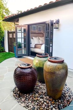 two large vases sitting on top of a gravel covered ground next to a bed